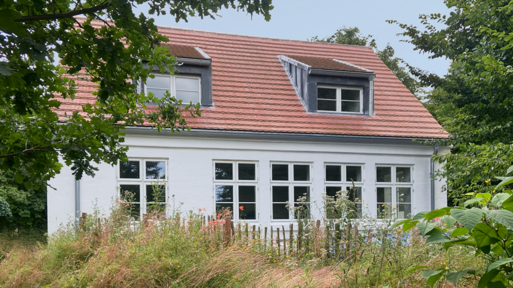 Weiß gestrichenes Steinhaus mit rotem Ziegeldach und Fensterreihe.